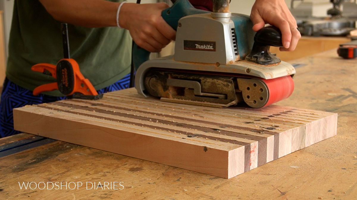 using a belt sander to flatten cutting board on workbench