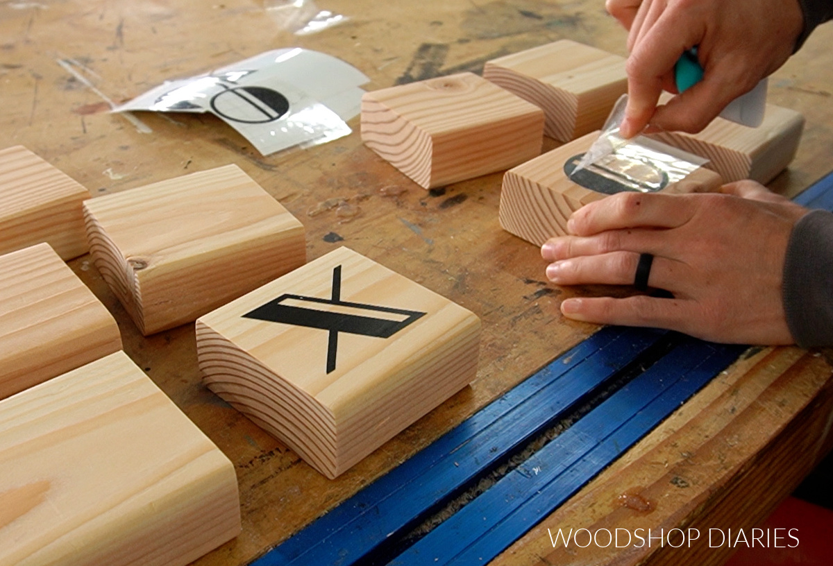Applying vinyl Xs and Os to 2x4 game board blocks on workbench