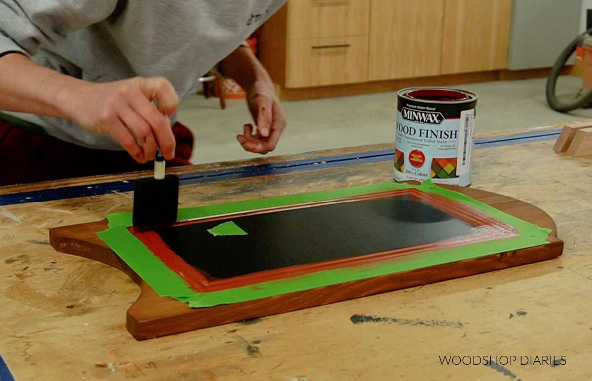 Shara Woodshop Diaries applying red stain to stencil on wooden sled seat board