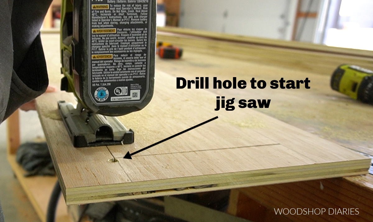 Jig saw cutting out drawer opening in side panels--arrow pointing to the hole drilled outside the line to start the blade from