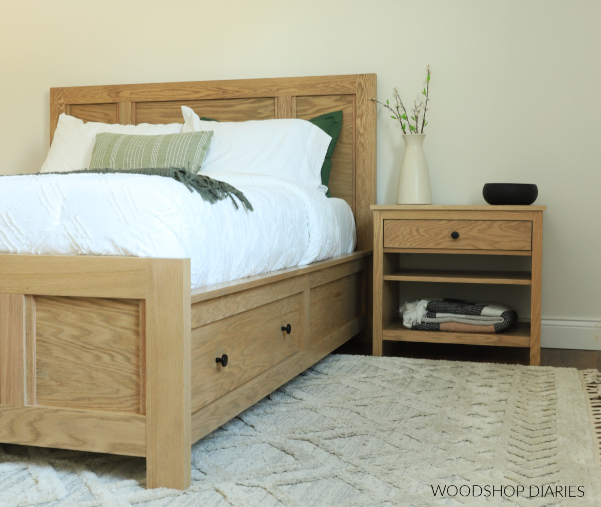 Red oak modern nightstand sitting next to DIY storage bed in bedroom with vase on top and blanket on bottom shelf