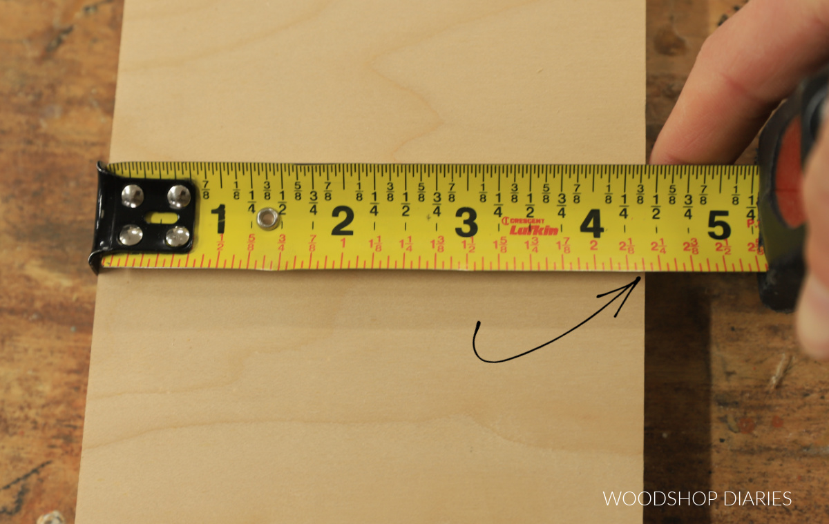 Tape measure stretched across board with arrow pointing to self centering marks on tape
