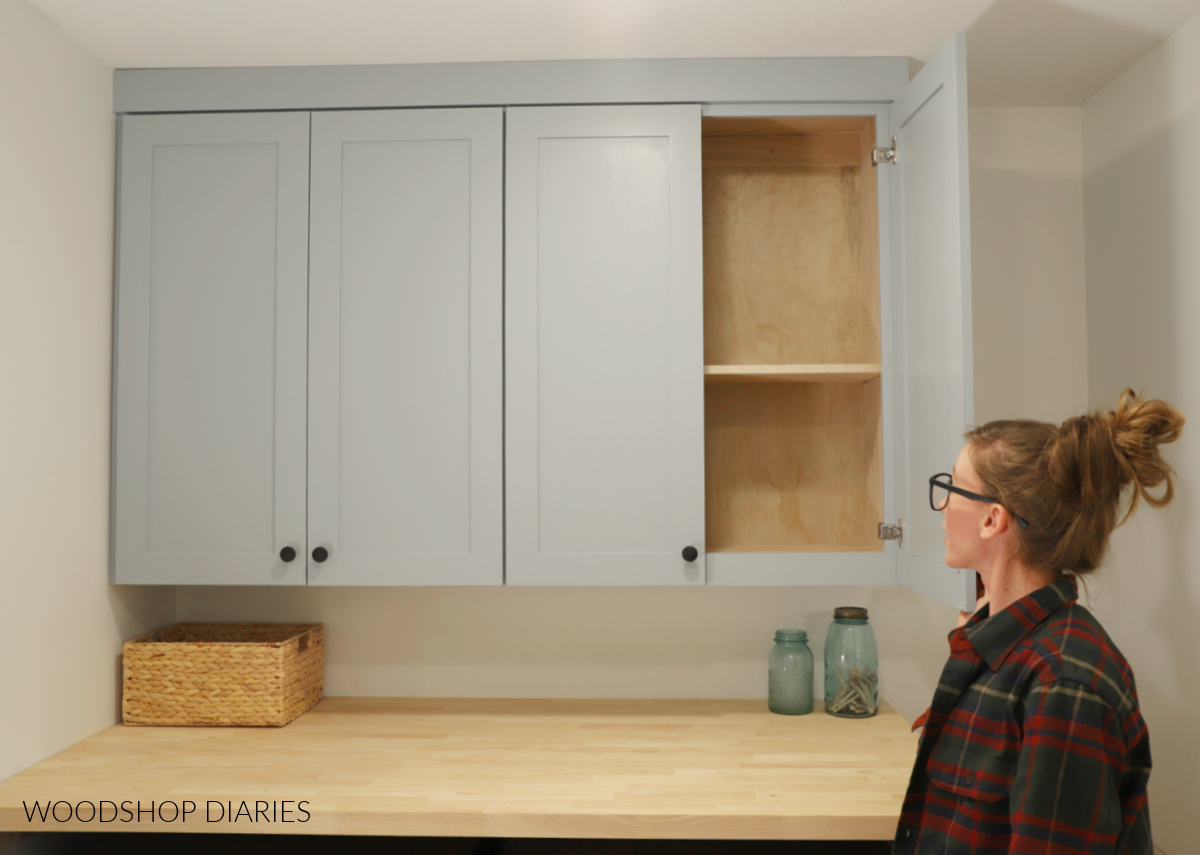 Shara Woodshop Diaries opening doors on wall cabinets above washer and dryer