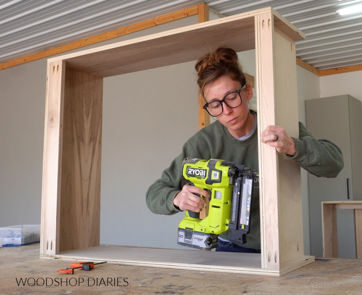 Shara Woodshop Diaries brad nailing bottom panel to bottom support of upper cabinet box on workbench