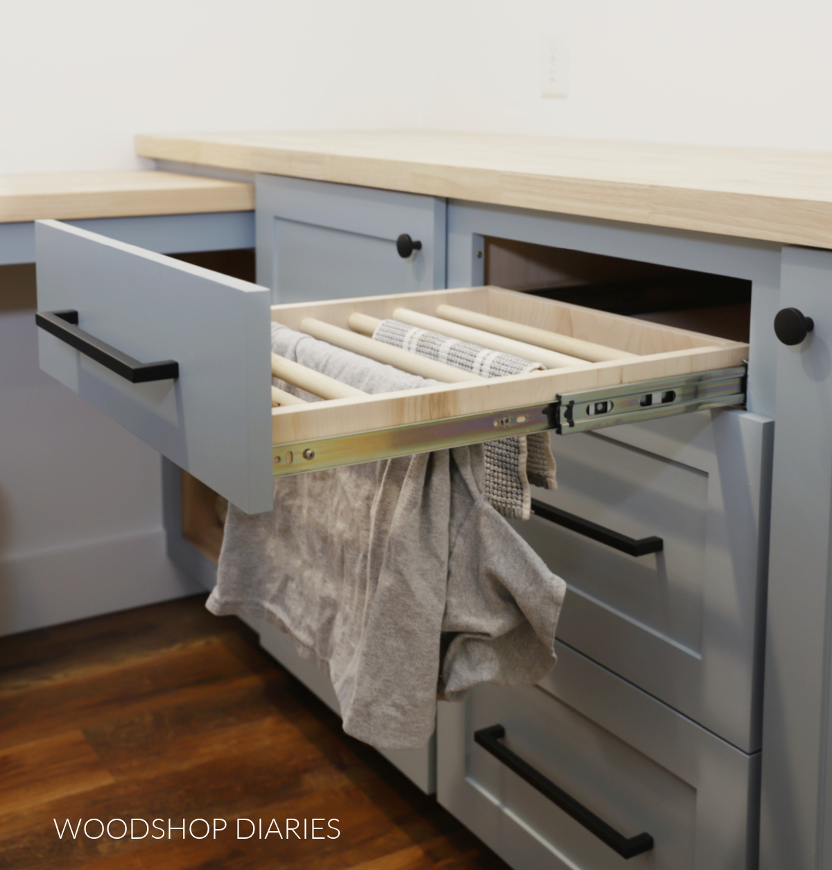 Completed drying rack drawer installed into base cabinet in laundry room with rag and shirt hanging from it