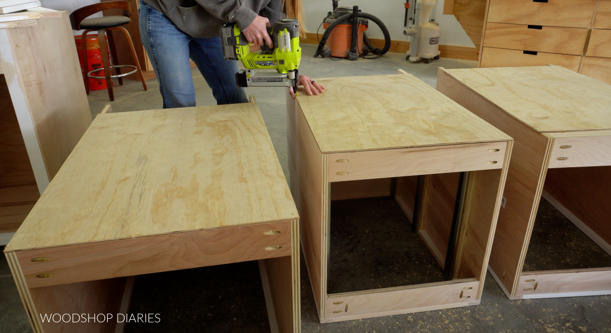 Shara Woodshop Diaries stapling back panel on base cabinets in workshop