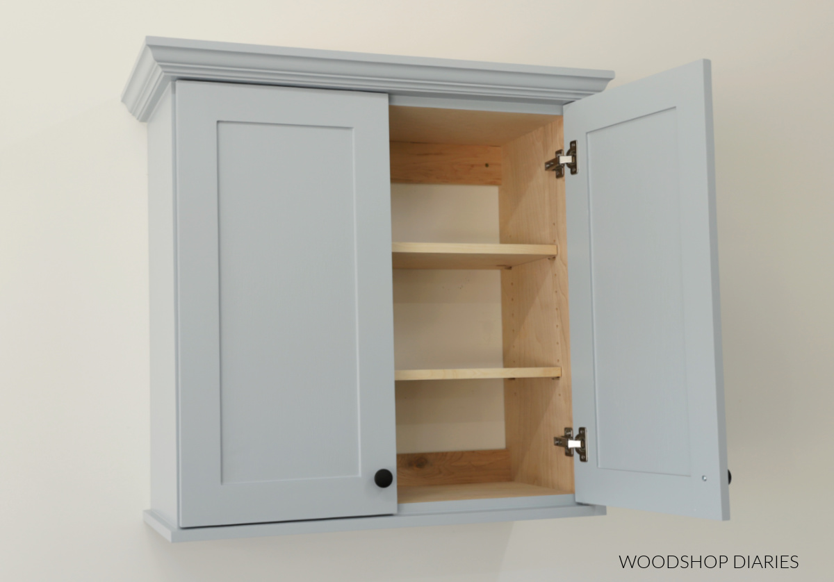 Bathroom wall cabinet with double doors. One door open to reveal two adjustable shelves inside