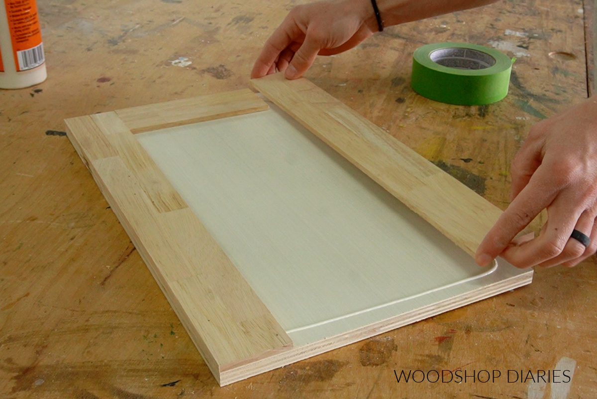 Shara Woodshop Diaries gluing lattice trim piece onto front of ½" plywood panel on workbench