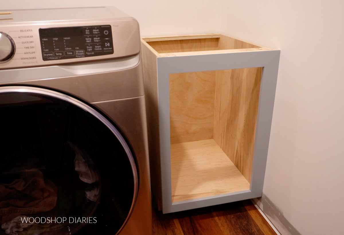open base cabinet installed next to washing machine in corner of laundry room