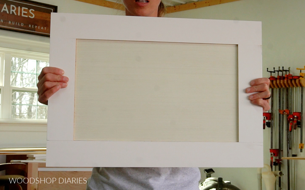 Shara Woodshop Diaries holding shaker style cabinet door up in workshop