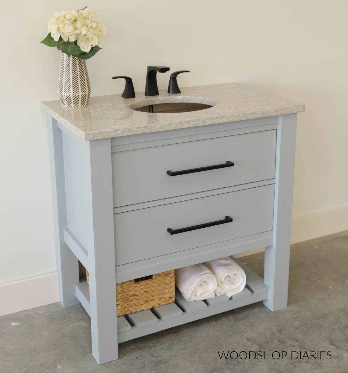 Small blue bathroom vanity with two large drawers and a slatted bottom shelf with granite top