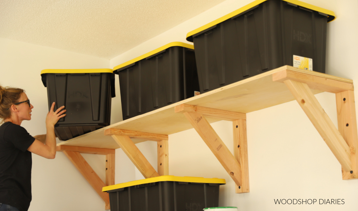 Shara Woodshop Diaries placing storage tote on garage wall shelves made from 2x4s and plywood