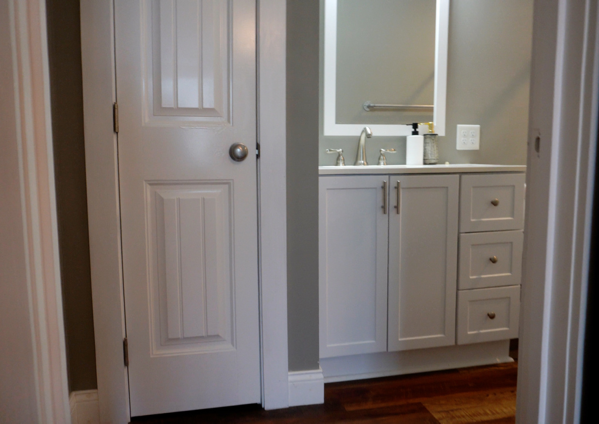 Bathroom before image showing existing closet in corner with white vanity on the right