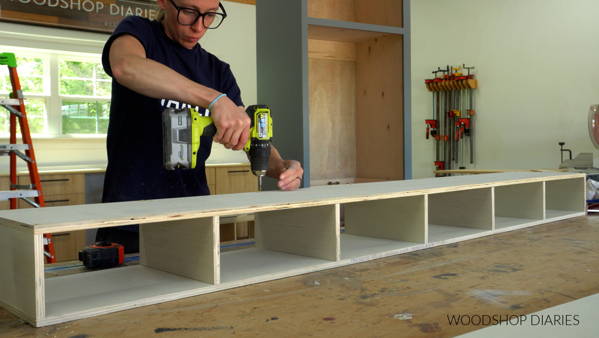 Shara Woodshop Diaries screwing together plywood cubby shelf on workbench for garage makeover