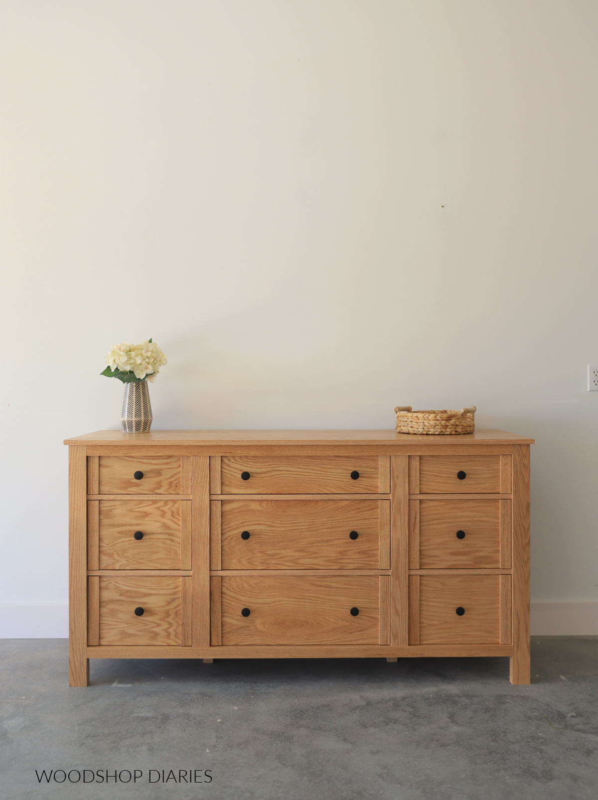 DIY completed red oak 9 drawer dresser against white wall with vase and flowers on top