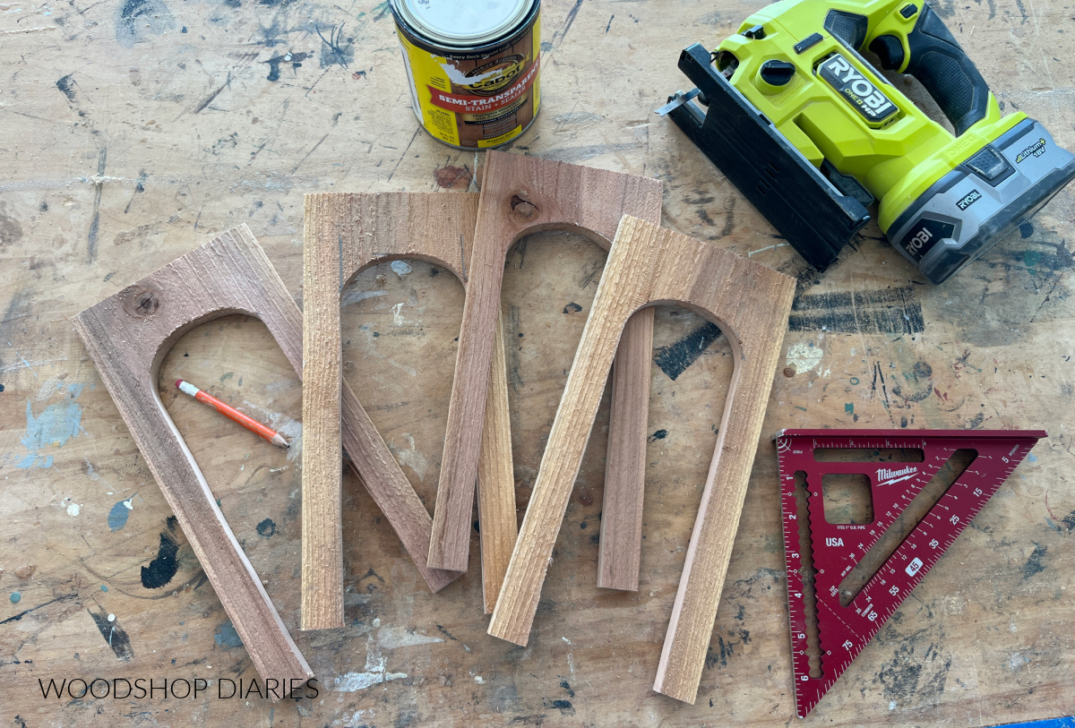 four fence pickets on workbench with arches cut out with jig saw, square, pencil, and stain can laying around