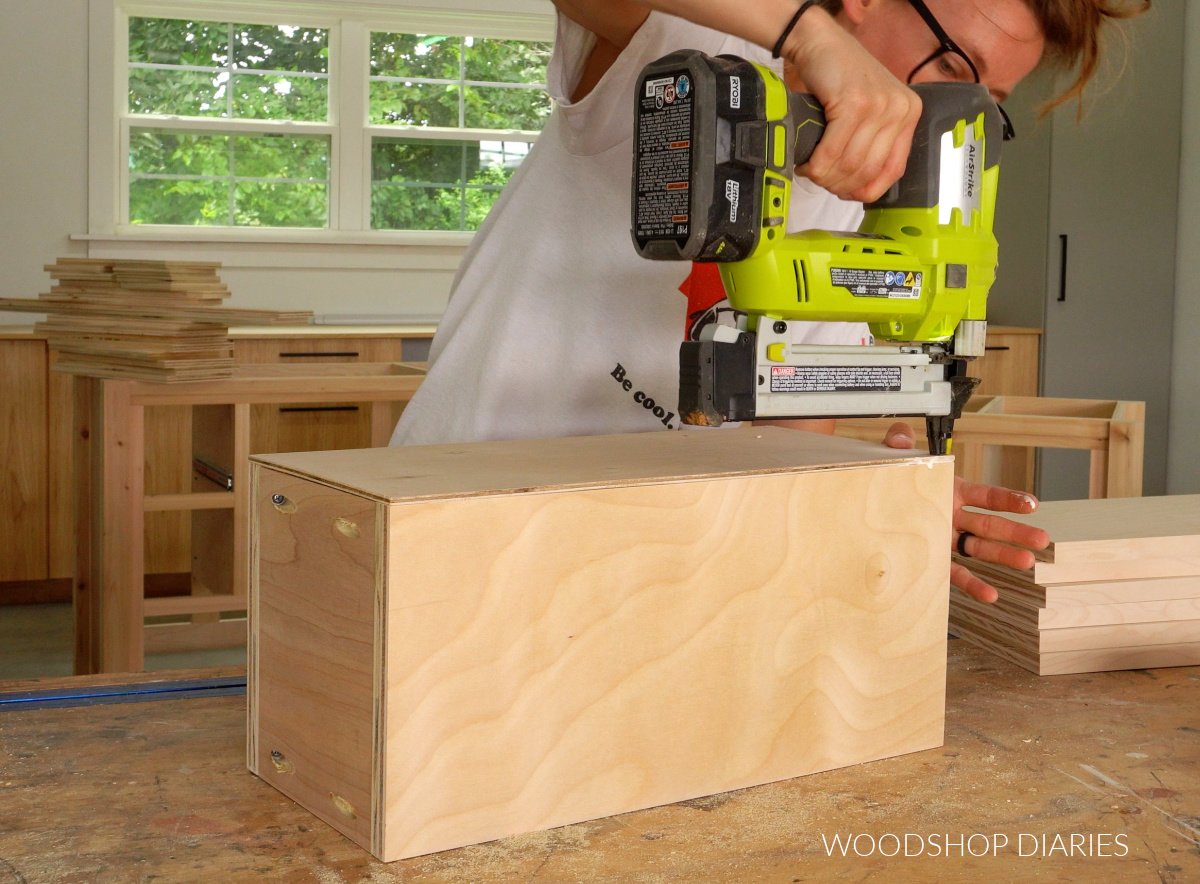 Shara Woodshop Diaries stapling bottom panel onto drawer box on workbench