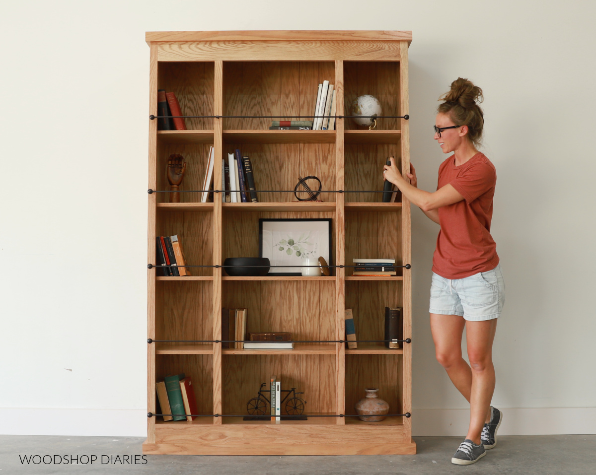 Shara Woodshop Diaries standing next to bookcase with shelf railing across five shelves
