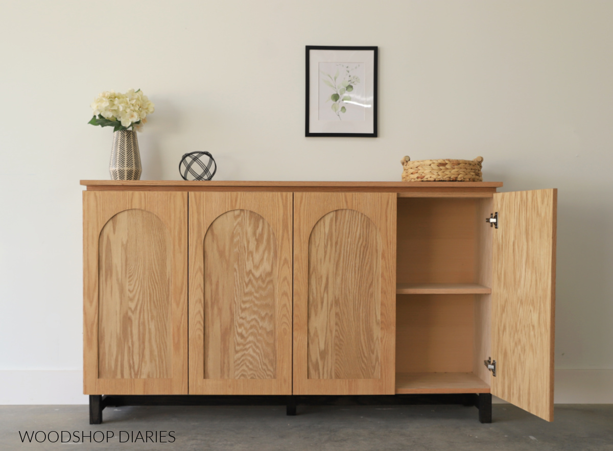 Completed DIY modern console cabinet with arched trim doors. Far right door open to reveal shelves inside