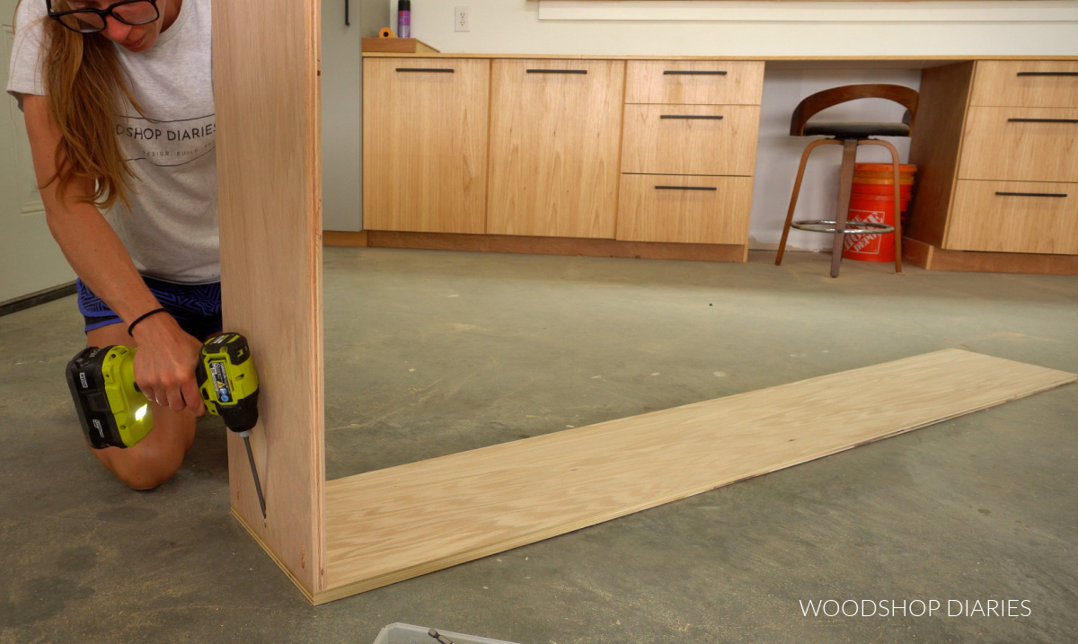 Shara Woodshop Diaries assembling top panel of bookcase to side panel on workshop floor