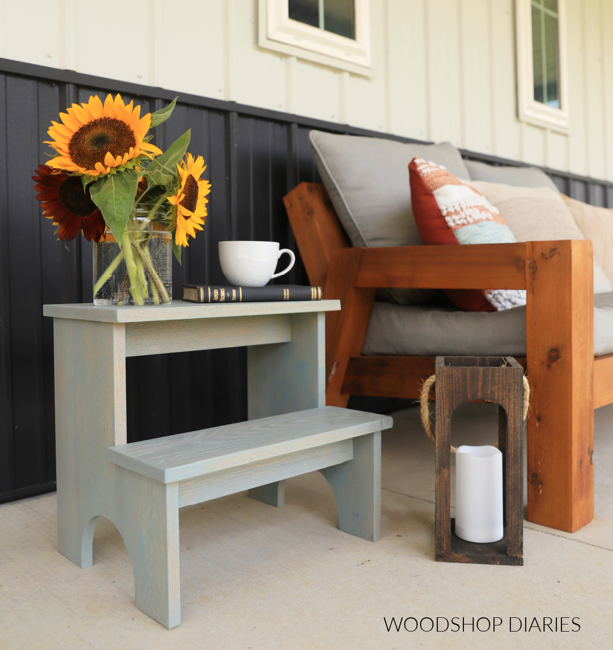 Green stained side table next to outdoor sofa with sunflowers in vase