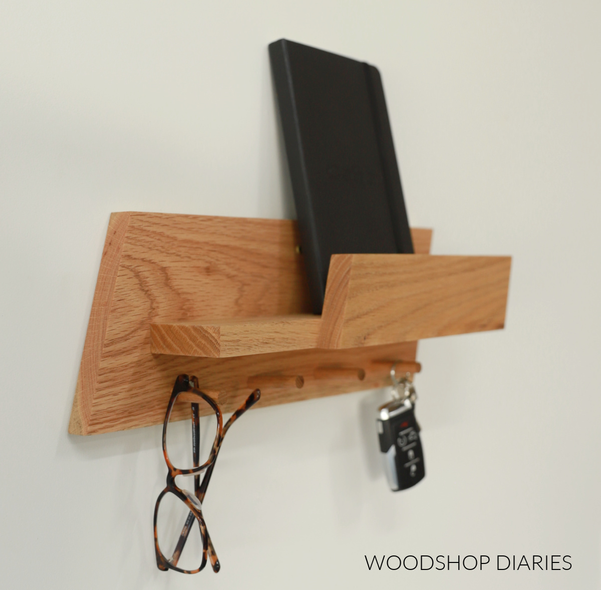 Close up of angled edge of entryway wall shelf with glasses and keys hanging on pegs