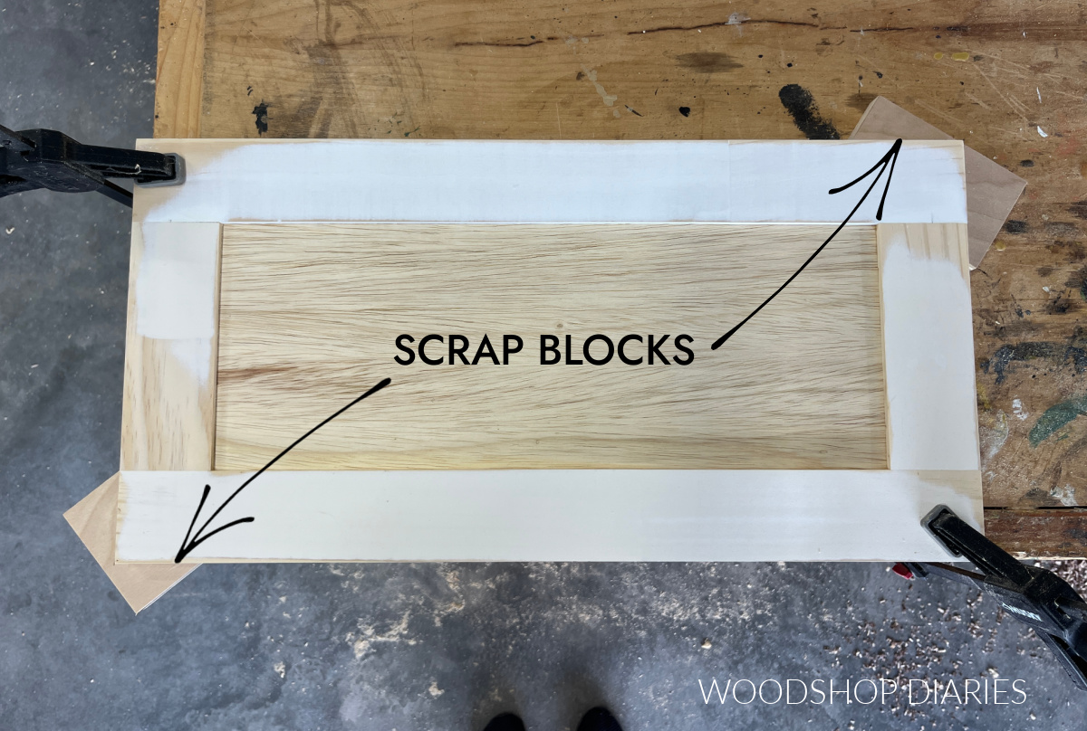 Overhead view of cabinet door placed on workbench on scrap blocks with clamps clamping opposite corners