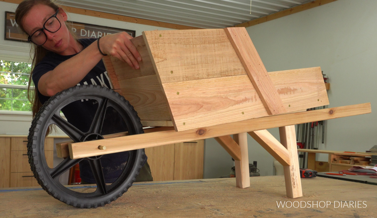 Placing wheelbarrow body on wheelbarrow supports on workbench