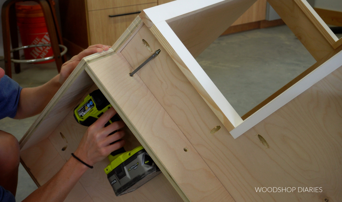 Driving screws to secure corner base cabinet face frame through access holes drilled in toe kick