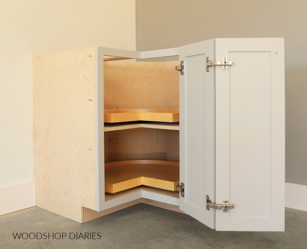 Corner base cabinet with bi-fold doors open revealing adjustable shelf inside with two lazy susans
