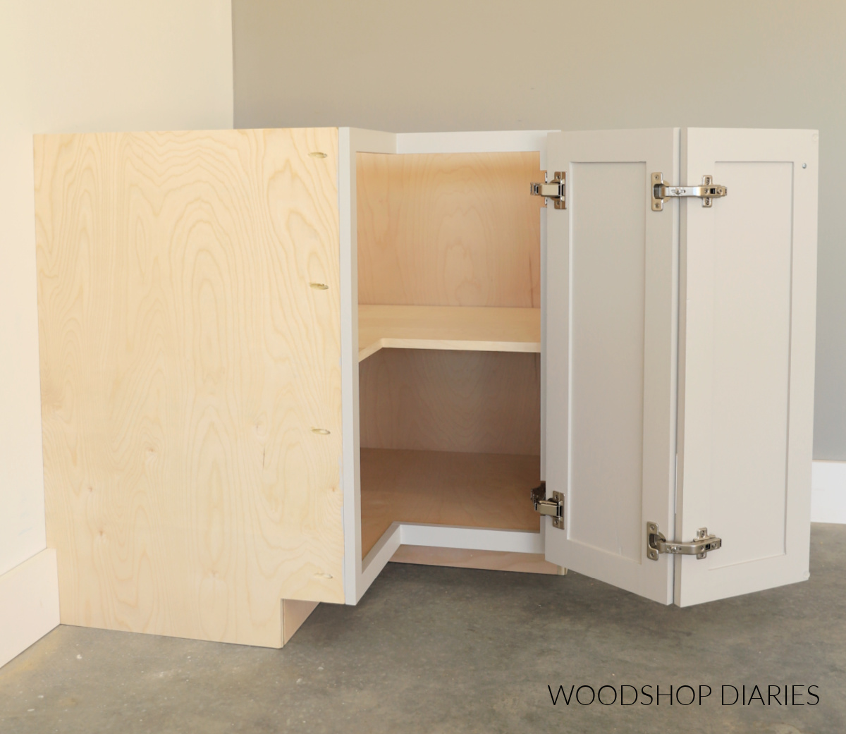 Completed DIY corner base cabinet with bi fold doors open revealing four hinges and a shelf inside