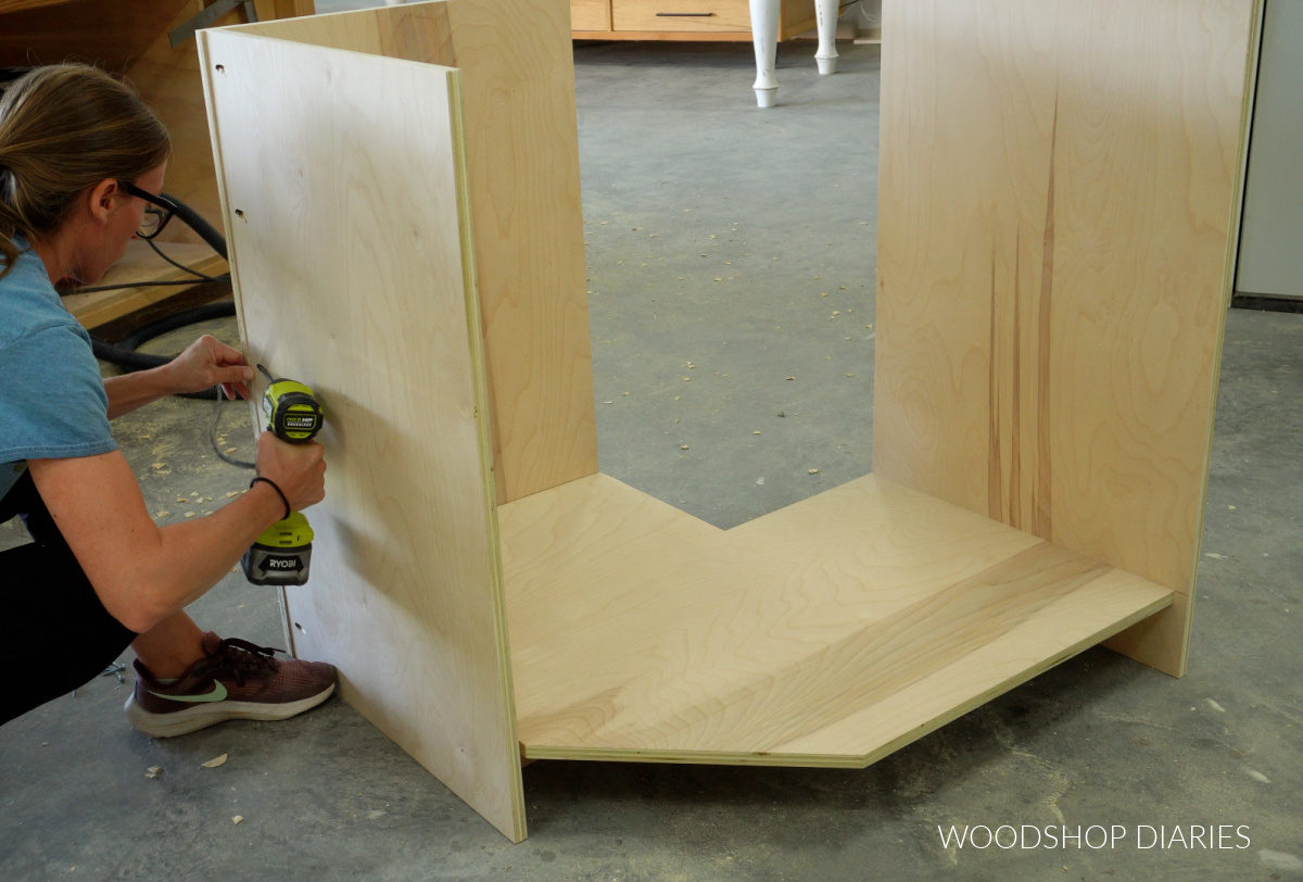 Shara Woodshop Diaries installing back panel of DIY corner cabinet with pocket holes on workshop floor