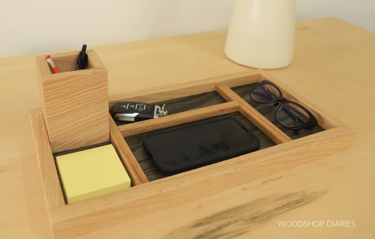 Wooden organizer tray with pencil holder cup and wooden dividers separating post it notes, phone, keys, glasses