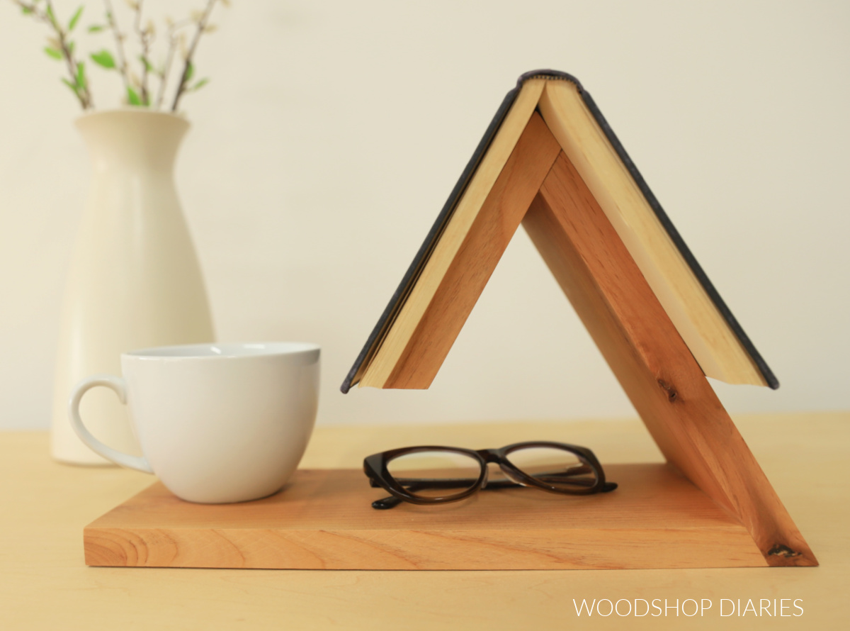 DIY book holder with open book on top and classes and mug on bottom