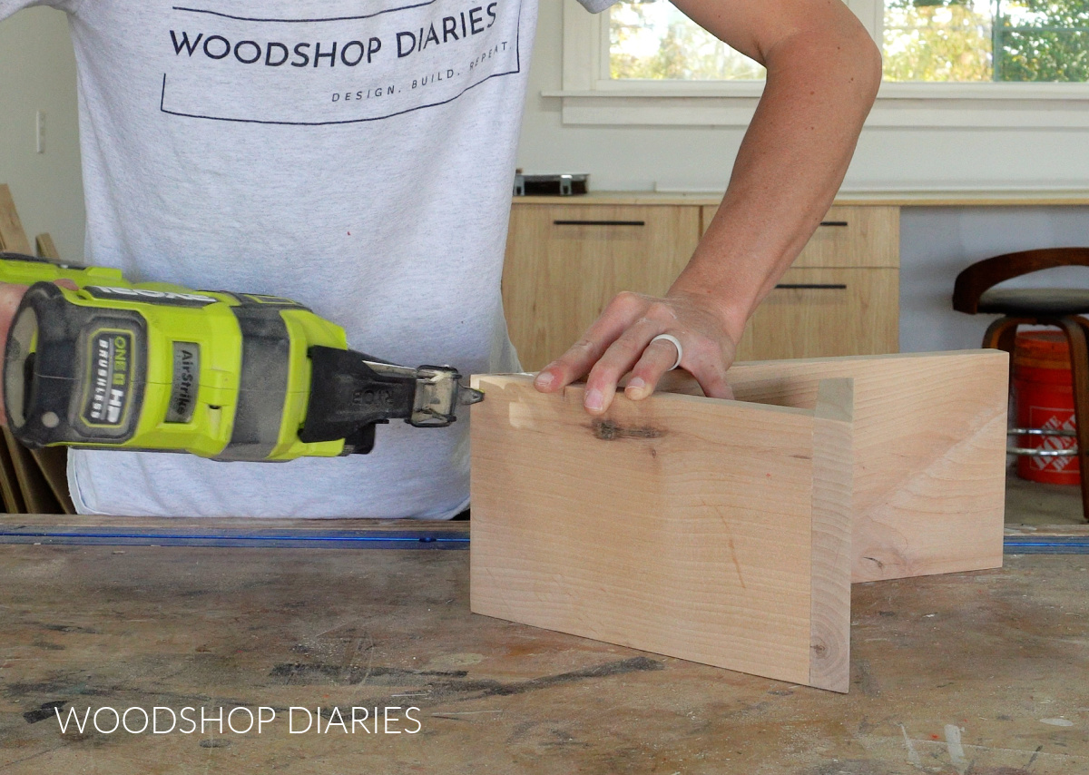 Shara Woodshop Diaries nailing book holder to bottom board on workbench