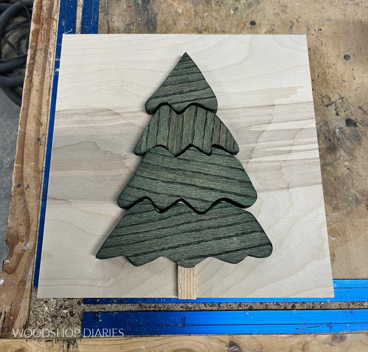 Christmas tree wood art pieces stained green and laid out on plywood backer