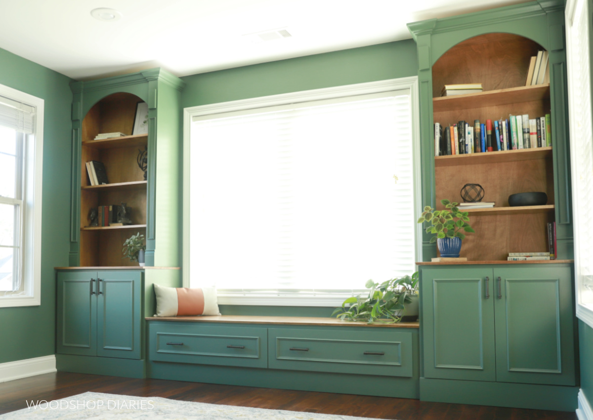 Built in cabinets with bookshelves and bench seat under window in office spanning wall to wall and painted green