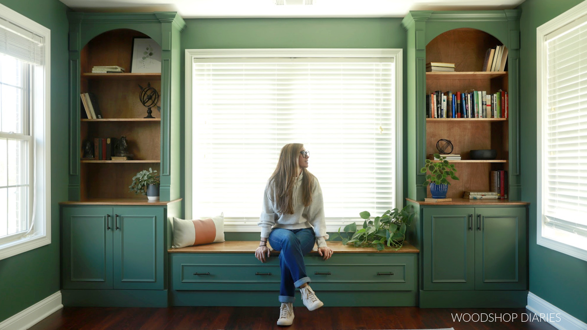 Shara Woodshop Diaries sitting on bench seat between DIY built in cabinets painted green with wood stained accents