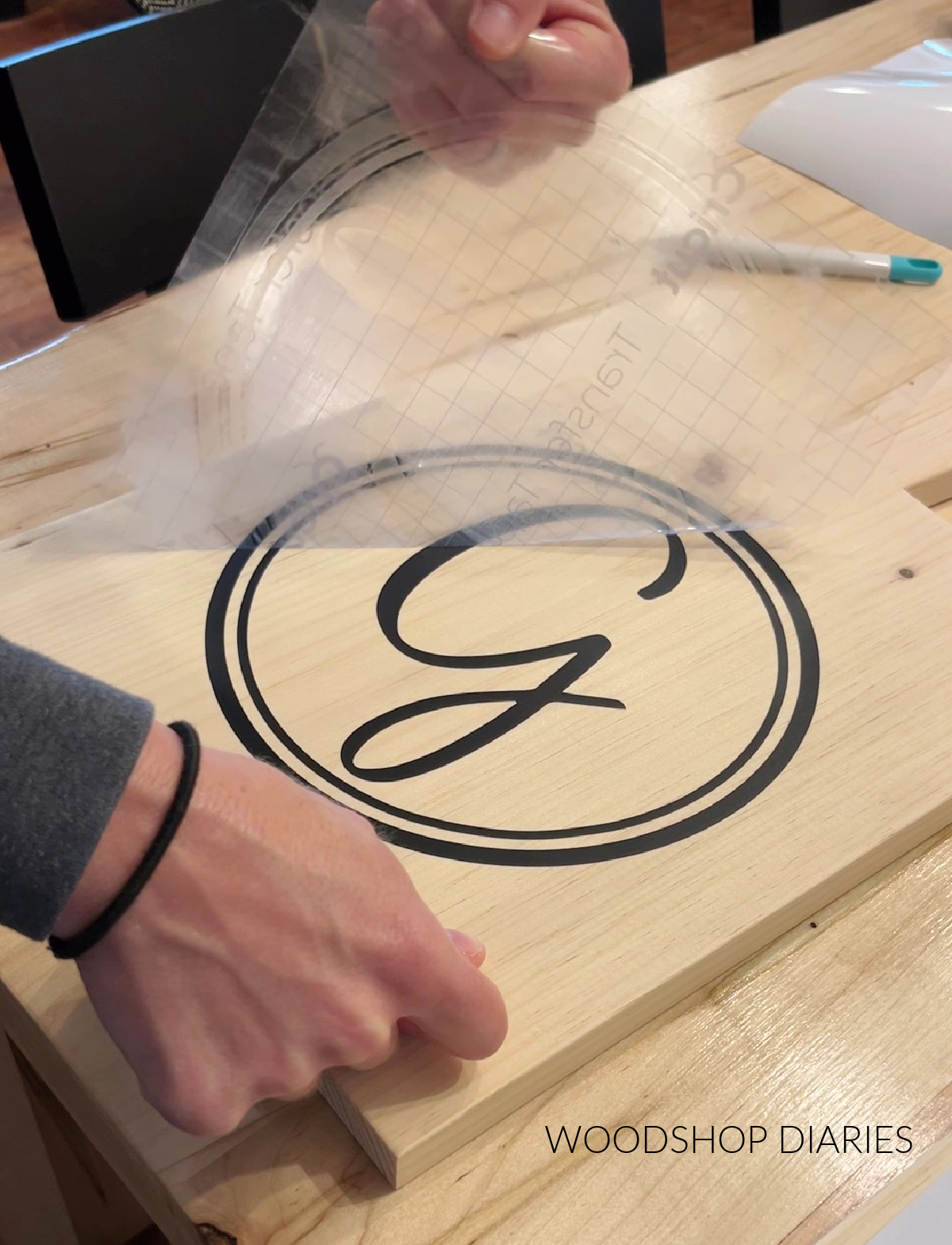 Shara Woodshop Diaries removing transfer tape after applying the vinyl stencil to one of the serving boards