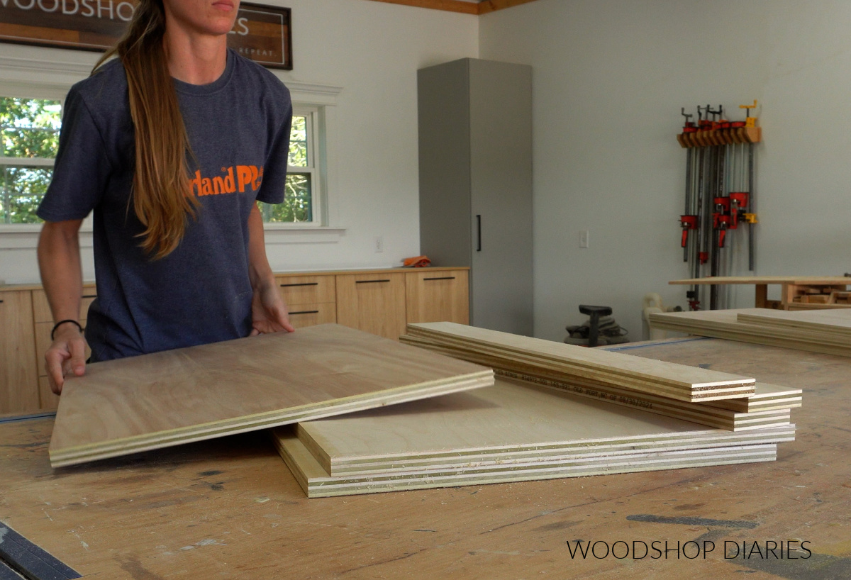 Shara Woodshop Diaries stacking plywood pieces on workbench to use for base cabinets