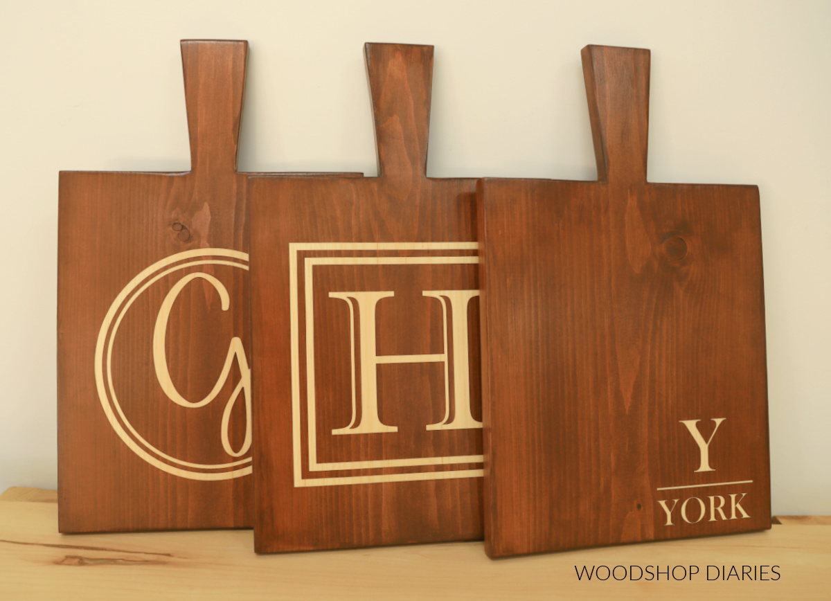 Three wooden serving boards personalized with wood stain--one with round monogram, one with square monogram, and one with bottom corner last name