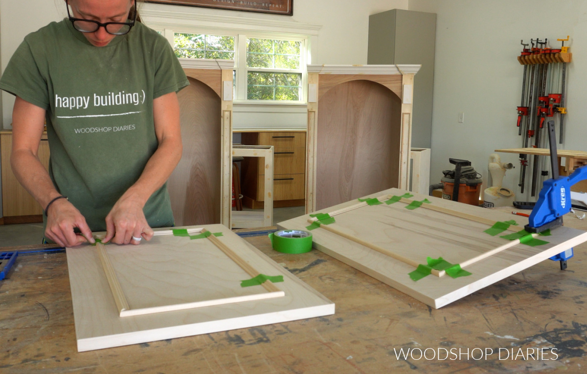Shara Woodshop Diaries gluing and taping molding onto front of cabinet doors on workbench