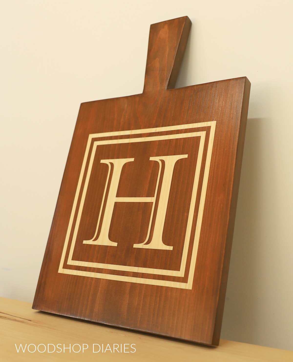 Close up of monogrammed serving board with handle. Monogram "H" is stained into the board