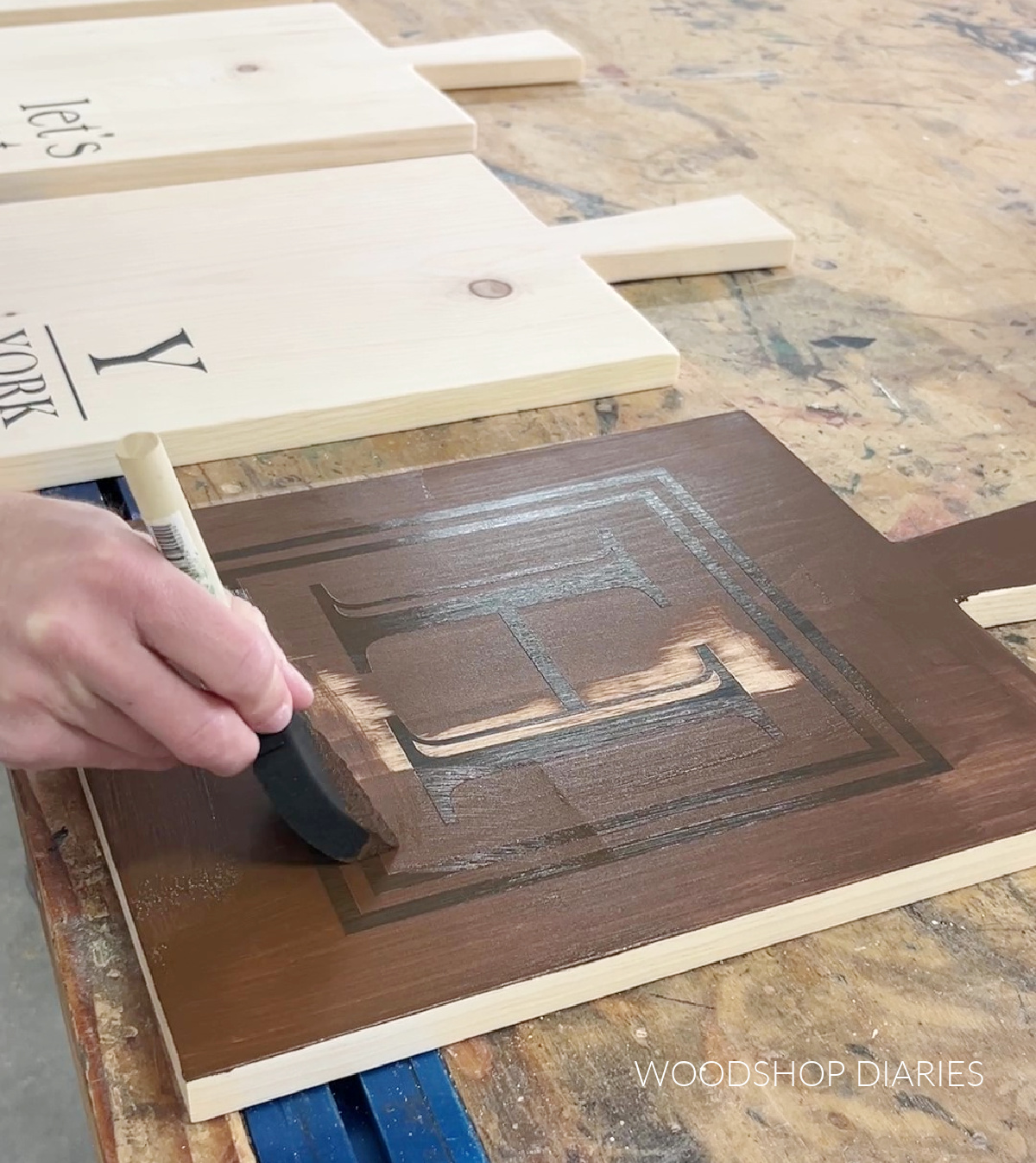 Applying wood stain with a foam brush to serving board with vinyl stencil in place