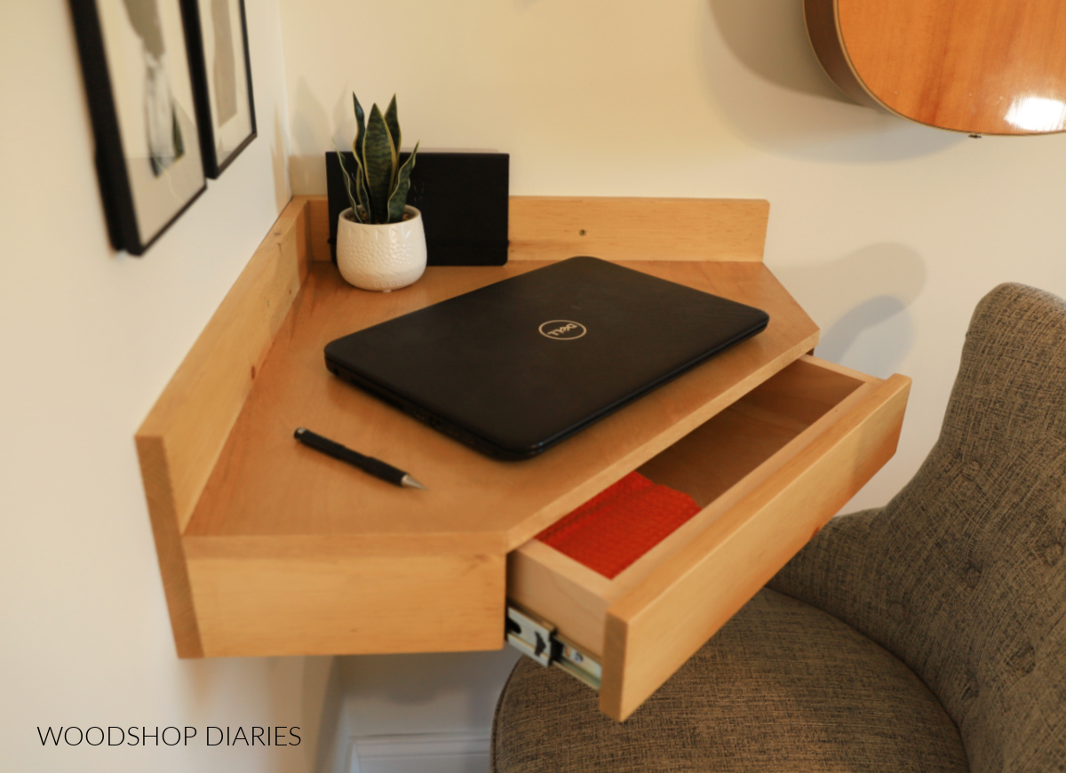 Floating corner desk hung on wall with drawer open and laptop setting on it