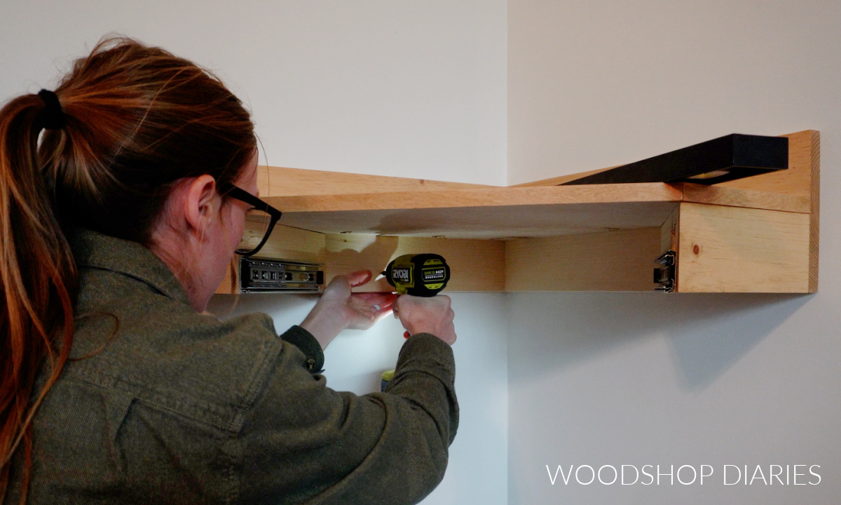 Shara Woodshop Diaries driving screws to hang floating corner desk on wall