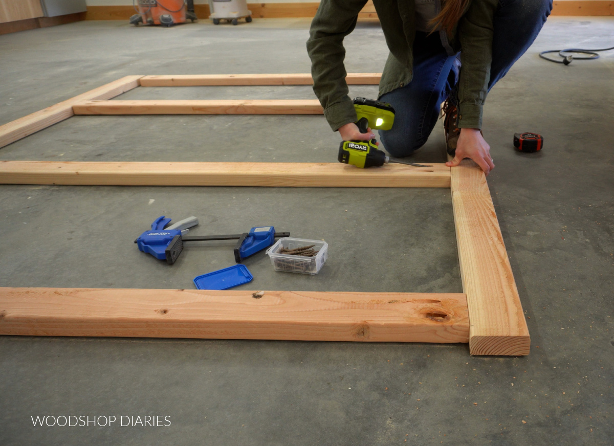 Shara Woodshop Diaries driving screws in pocket holes to assemble front and back shelf frames on concrete workshop floor
