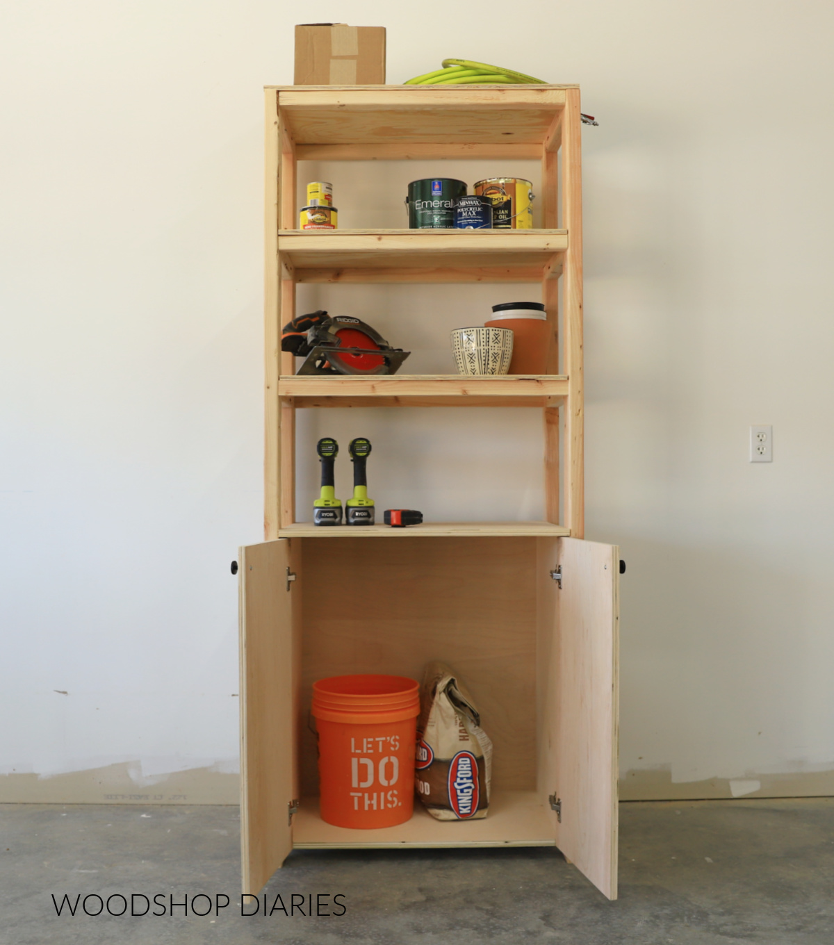 Completed wooden garage shelf with built in cabinet--cabinet doors open with bucket and bag of charcoal inside