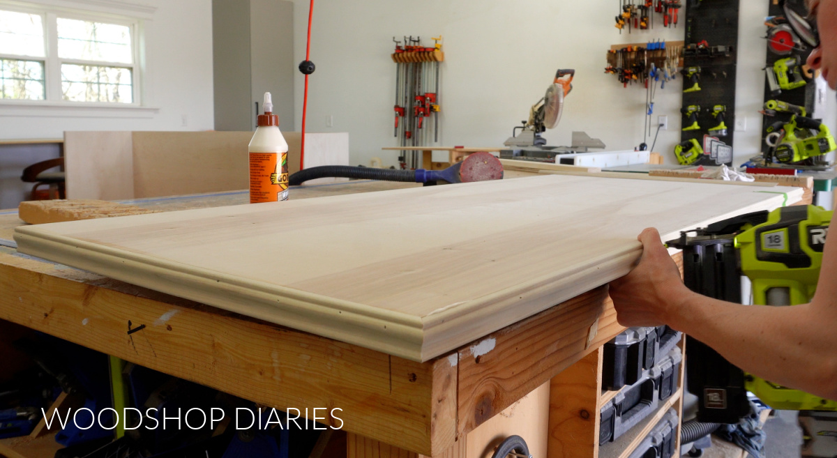 Plywood panel on workbench--Shara Woodshop Diaries nailing base cap molding around egdes with brad nailer 