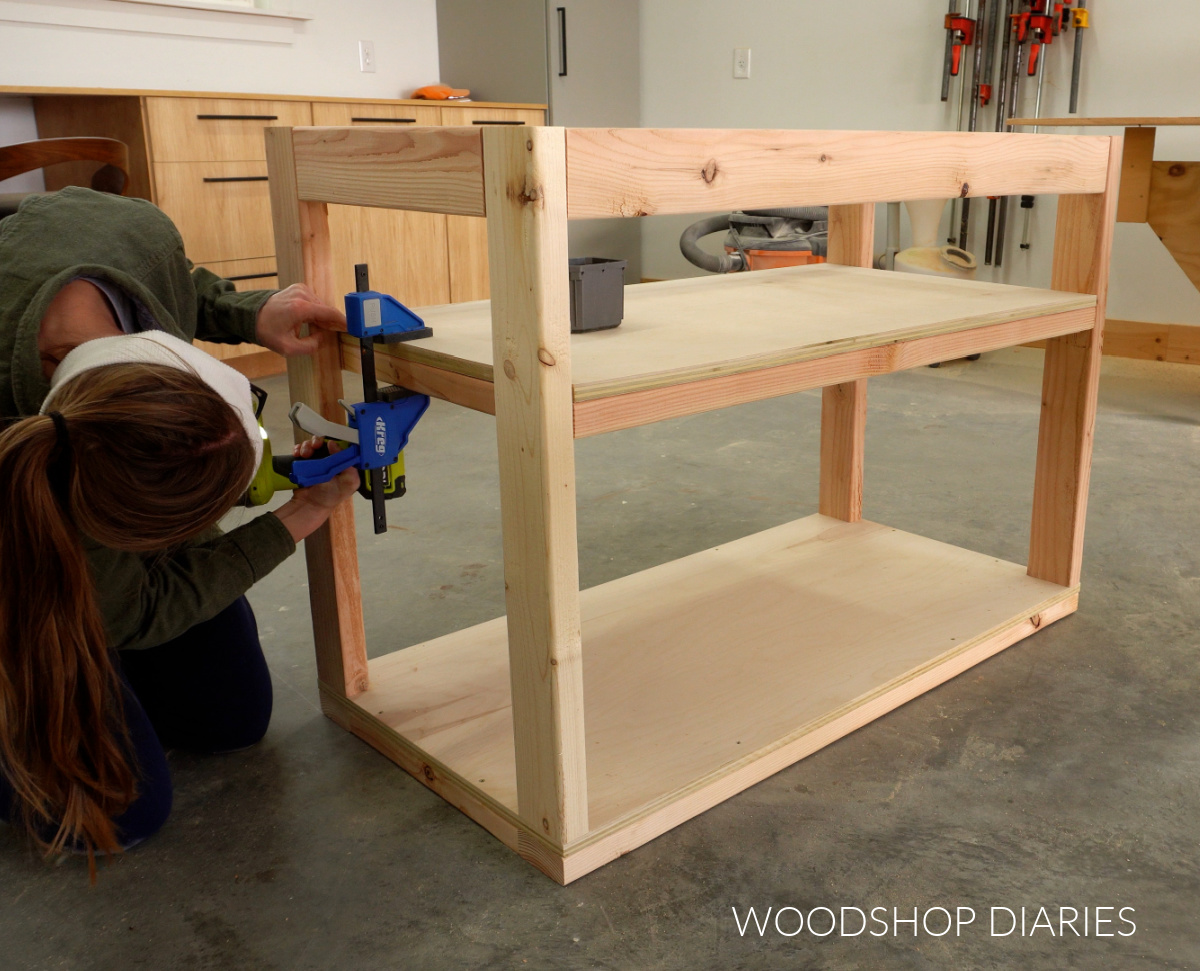 Shara Woodshop Diaries screwing plywood shelf into small DIY workbench
